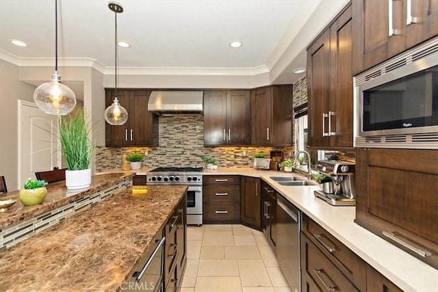 kitchen with wall chimney range hood, a sink, appliances with stainless steel finishes, dark brown cabinetry, and backsplash