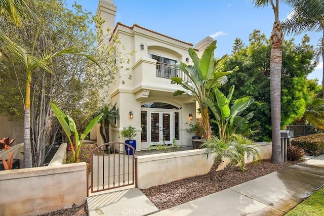view of front of property with stucco siding, a fenced front yard, a gate, french doors, and a balcony