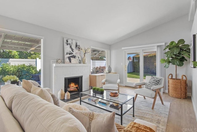 living room featuring light wood-style floors, a brick fireplace, and vaulted ceiling