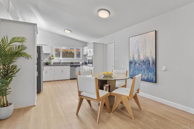 dining space featuring light wood finished floors, baseboards, and lofted ceiling