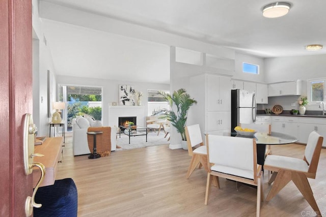 dining space featuring a lit fireplace, light wood-type flooring, and vaulted ceiling