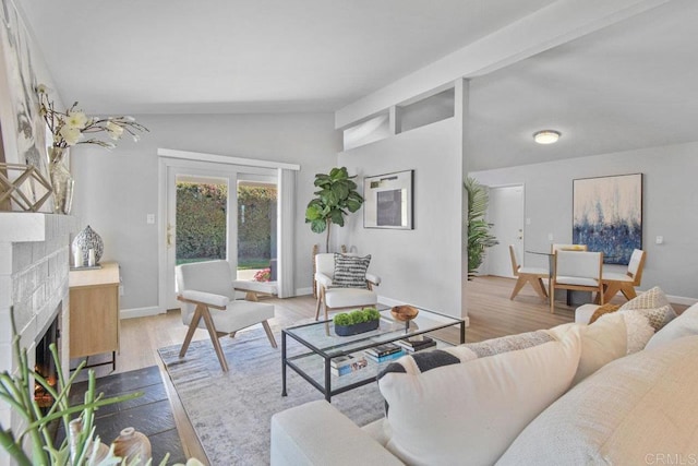 living area featuring a fireplace with flush hearth, baseboards, vaulted ceiling with beams, and wood finished floors