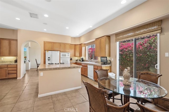 kitchen featuring a center island, light tile patterned flooring, white appliances, arched walkways, and visible vents