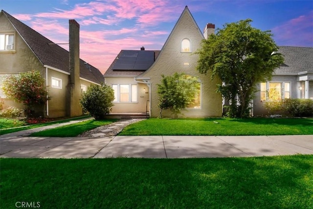 view of front facade featuring stucco siding, a chimney, a lawn, and roof mounted solar panels