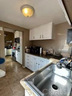 kitchen featuring stainless steel electric range, white cabinetry, a sink, and dark countertops