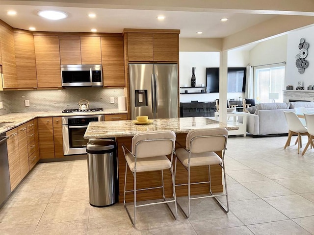 kitchen featuring brown cabinets, a center island, stainless steel appliances, tasteful backsplash, and a kitchen bar