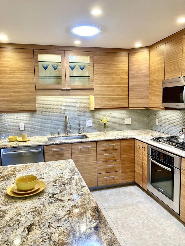 kitchen featuring decorative backsplash, light stone countertops, a sink, light tile patterned floors, and stainless steel appliances