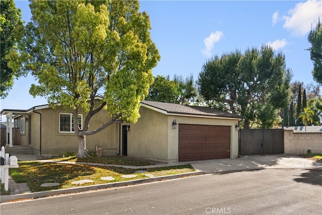 ranch-style house featuring an attached garage, fence, stucco siding, a gate, and driveway