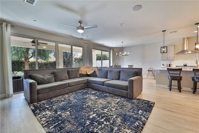 living area featuring light wood-style flooring, baseboards, and ceiling fan with notable chandelier