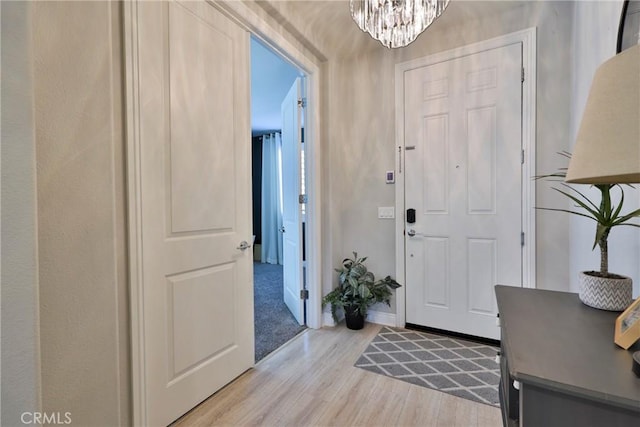 foyer entrance with baseboards, light wood finished floors, and a chandelier