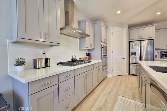 kitchen featuring light wood-style flooring, gray cabinetry, wall chimney exhaust hood, and stainless steel appliances