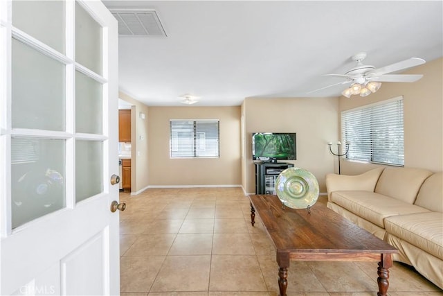 living area with light tile patterned flooring, visible vents, a ceiling fan, and baseboards