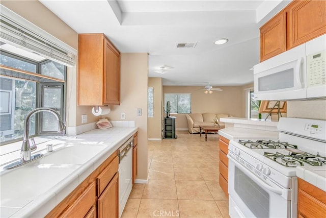 kitchen featuring a sink, tile countertops, white appliances, ceiling fan, and visible vents