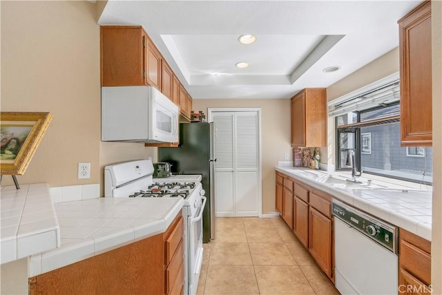 kitchen featuring recessed lighting, a raised ceiling, tile countertops, and white appliances