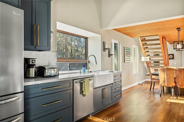 kitchen featuring tasteful backsplash, dark wood-style flooring, baseboards, stainless steel appliances, and a sink