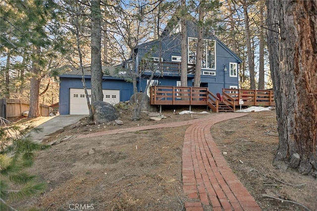 rear view of property featuring driveway, a wooden deck, fence, and an attached garage