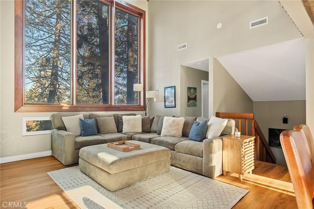 living area with visible vents, baseboards, high vaulted ceiling, and wood finished floors