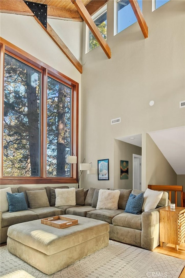 living area with high vaulted ceiling, visible vents, beamed ceiling, and wood finished floors