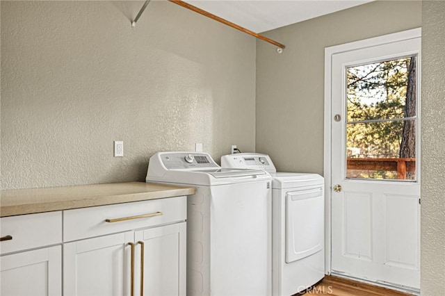 clothes washing area featuring separate washer and dryer, a textured wall, and cabinet space
