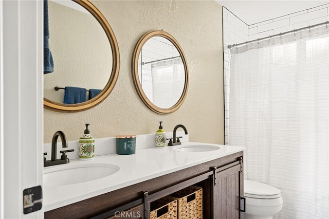 bathroom featuring a textured wall, double vanity, a sink, and toilet