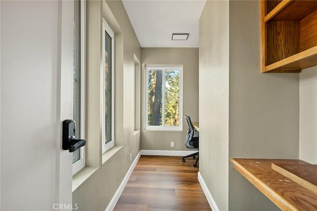 hall featuring a textured wall, baseboards, and wood finished floors