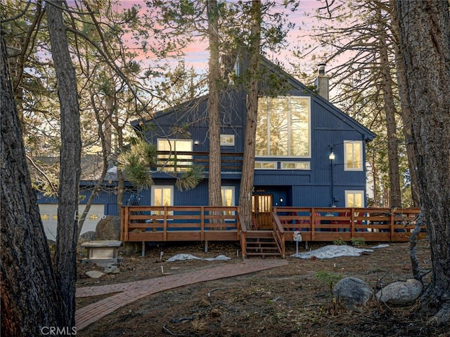 back of house at dusk with a chimney and a wooden deck