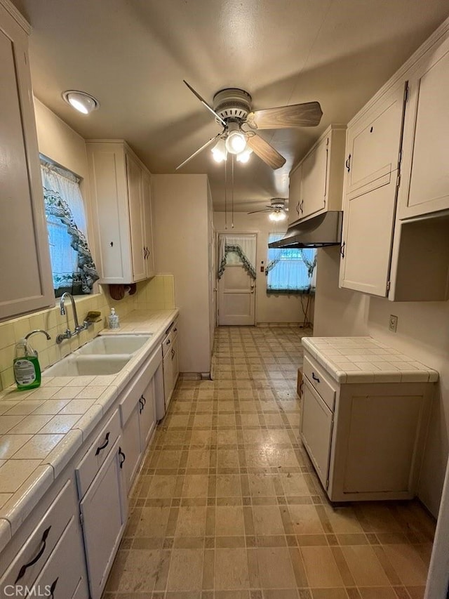 kitchen featuring tile countertops, white cabinets, and a sink