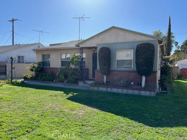 view of front facade with stucco siding, brick siding, fence, and a front yard