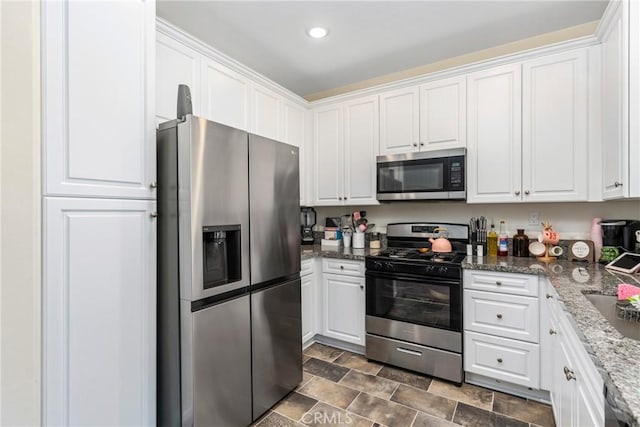kitchen with dark stone countertops, recessed lighting, white cabinetry, appliances with stainless steel finishes, and stone finish flooring