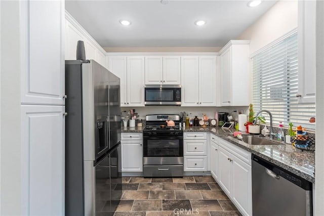 kitchen featuring recessed lighting, white cabinetry, dark stone counters, appliances with stainless steel finishes, and a sink