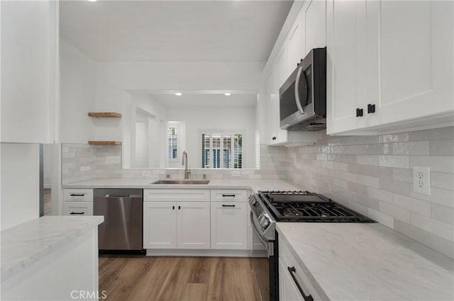 kitchen with light stone countertops, open shelves, appliances with stainless steel finishes, a sink, and decorative backsplash