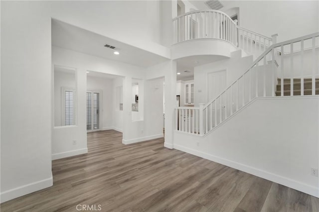 unfurnished living room with stairs, visible vents, baseboards, and wood finished floors