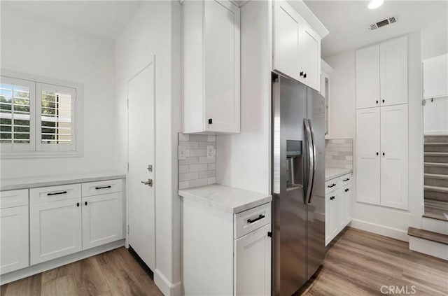 kitchen featuring light wood-type flooring, light countertops, white cabinetry, stainless steel refrigerator with ice dispenser, and visible vents