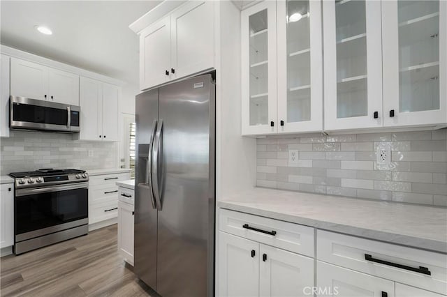 kitchen featuring glass insert cabinets, white cabinets, appliances with stainless steel finishes, light wood-type flooring, and backsplash