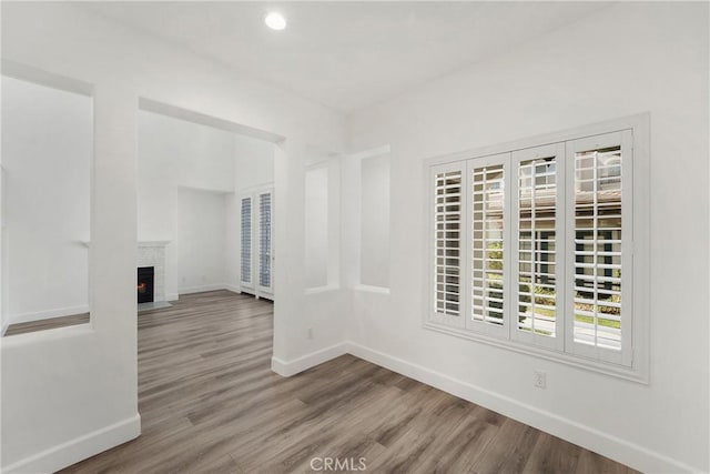 spare room featuring wood finished floors, a fireplace, baseboards, and recessed lighting
