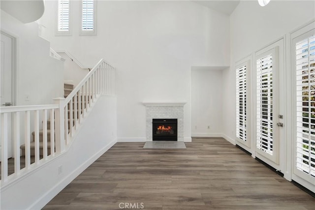 unfurnished living room featuring a towering ceiling, baseboards, a fireplace, stairs, and wood finished floors