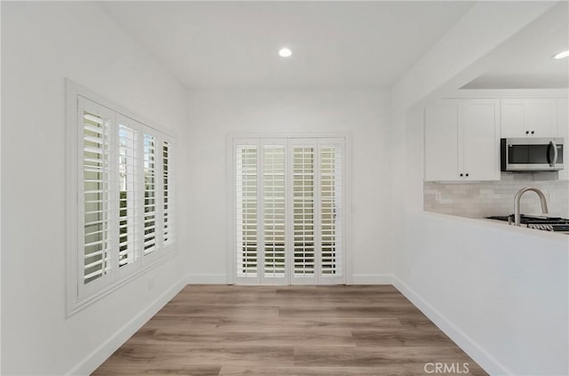 unfurnished dining area featuring a sink, baseboards, light wood finished floors, and recessed lighting