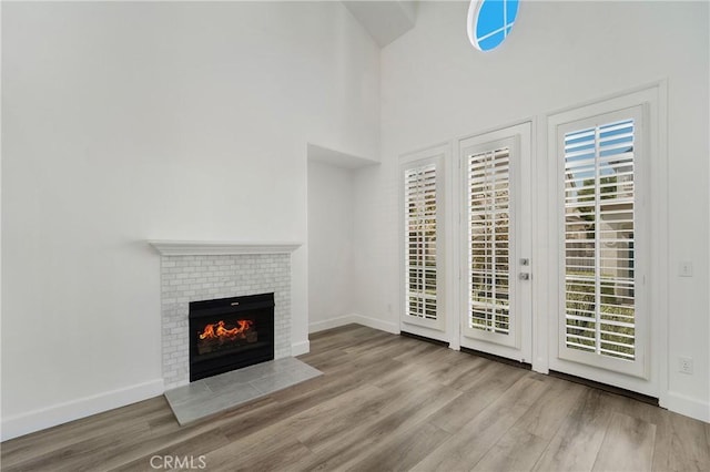 unfurnished living room featuring baseboards, a high ceiling, wood finished floors, and a fireplace