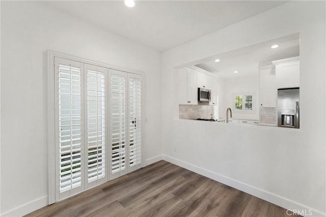 unfurnished dining area with a sink, baseboards, recessed lighting, and wood finished floors