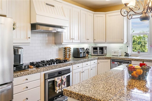 1251 Kodiak Dr, Lake Arrowhead, CA 92352 - kitchen with appliances with stainless steel finishes, wall chimney range hood, tasteful backsplash, white cabinets, and a chandelier
