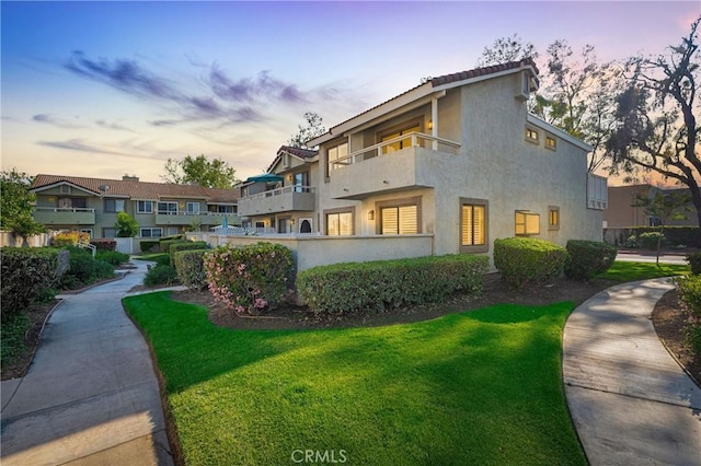 exterior space featuring a yard, a tiled roof, a balcony, and stucco siding