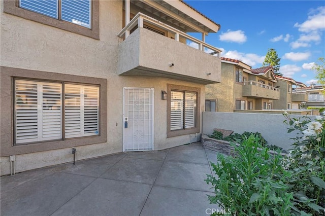 entrance to property with a patio, stucco siding, and fence