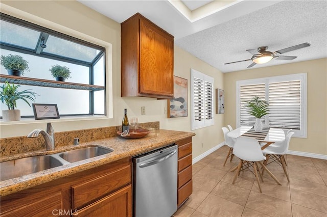 kitchen with dishwasher, a sink, a textured ceiling, brown cabinetry, and light stone countertops