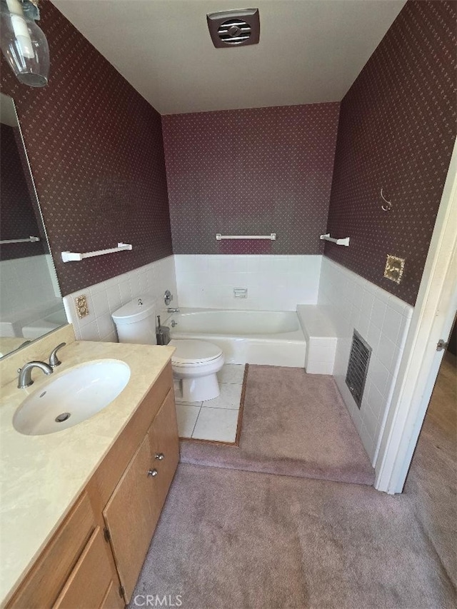 bathroom featuring wallpapered walls, a bathtub, toilet, a tiled fireplace, and vanity