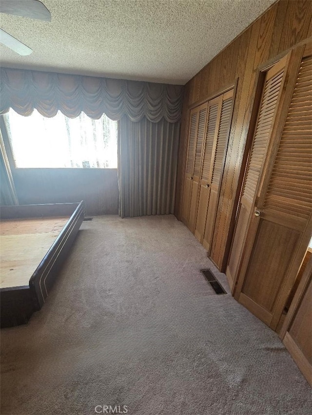 unfurnished bedroom featuring carpet, two closets, visible vents, a textured ceiling, and access to outside