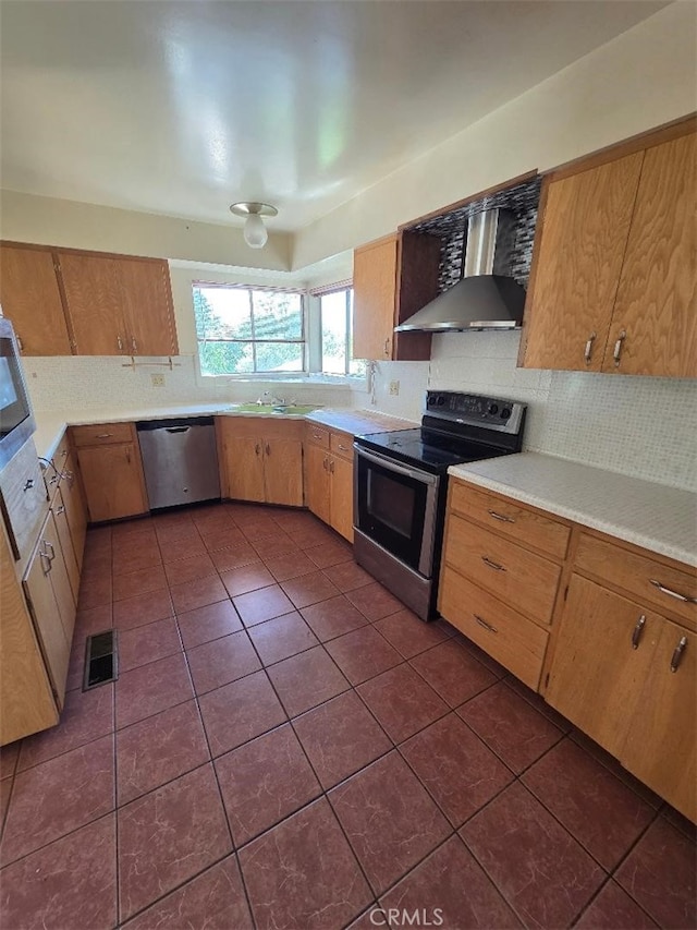 kitchen with wall chimney exhaust hood, dark tile patterned flooring, visible vents, backsplash, and appliances with stainless steel finishes
