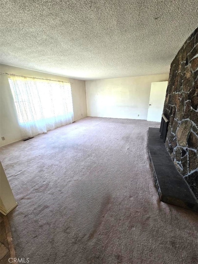 unfurnished living room with a textured ceiling, a stone fireplace, and carpet floors