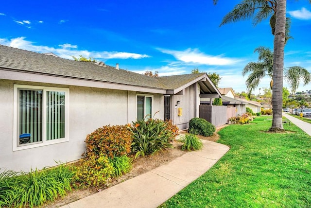 view of front of home featuring stucco siding, a shingled roof, a front yard, and fence