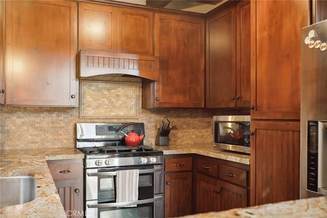 229 Chippewa Ln, Lake Arrowhead, CA 92352 - kitchen with appliances with stainless steel finishes, premium range hood, brown cabinetry, light stone countertops, and backsplash