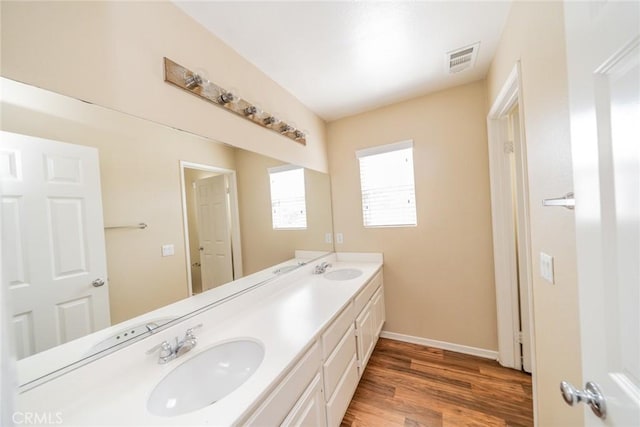 bathroom featuring baseboards, double vanity, visible vents, a sink, and wood finished floors